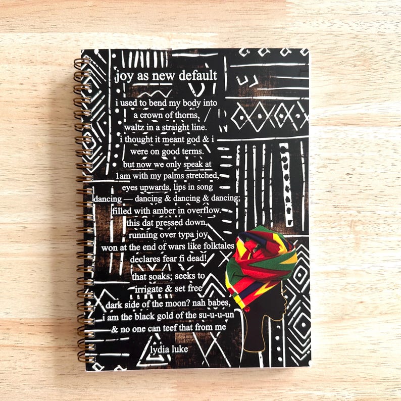 May include: A black and white spiral bound notebook with a colorful African print design and a quote that reads "joy as new default" by Lydia Luke.