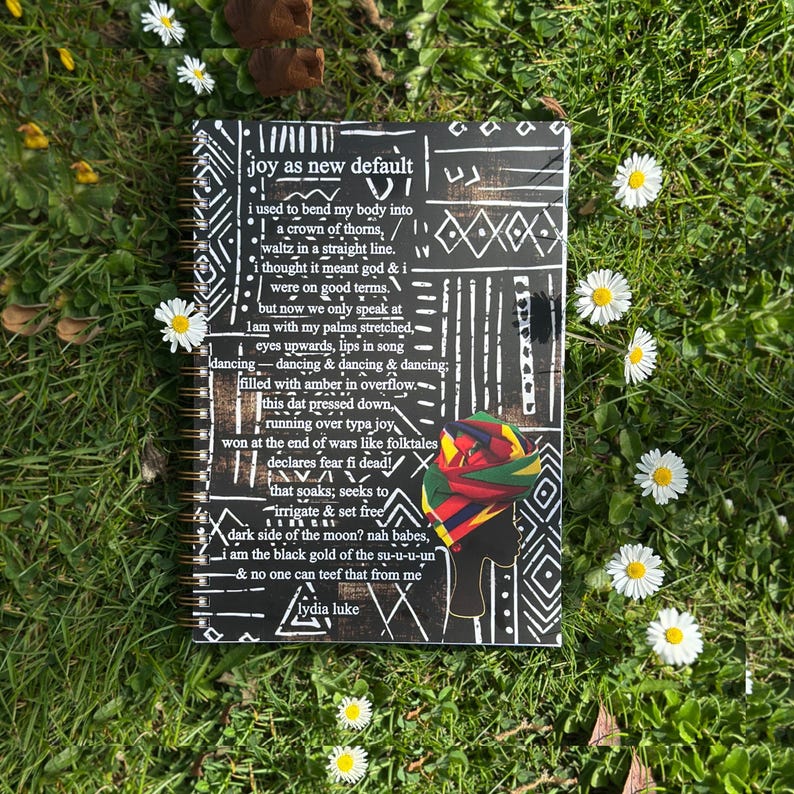 May include: A black and white notebook with a colorful patterned cover. The cover features a poem titled "joy as new default" by Lydia Luke. The poem is about finding joy in unexpected places.