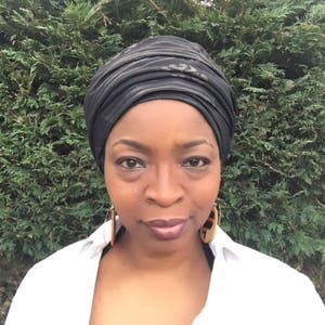 May include: A woman wearing a black head wrap with a white shirt. She has brown eyes and dark brown hair.