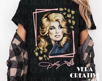May include: A black short-sleeve t-shirt featuring a graphic print of a blonde woman with voluminous hair, framed by a pink geometric border. The design includes green and tan leopard print accents, a small butterfly, and the script text Dolly.