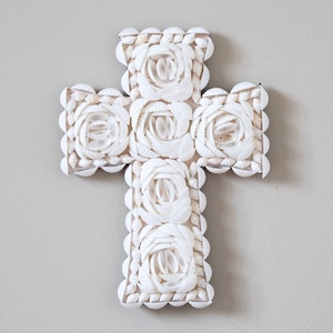 May include: White seashell cross with a floral design. The cross is made of many small seashells arranged in a pattern.