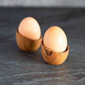 May include: Two brown wooden egg cups with a light brown egg in each.