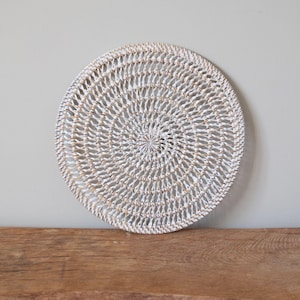 May include: White round woven placemat with a circular pattern. The placemat is made of natural materials and has a rustic look.