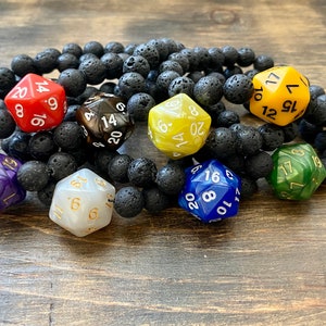 May include: A set of seven multi-colored dice bracelets with black lava rock beads. The dice are all 20-sided and have gold numbers.
