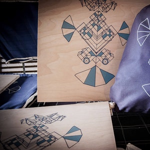 Könnte beinhalten: Zwei Holzstücke mit geometrischen Mustern darauf gedruckt. Die Muster sind in Schwarz und Blau auf einem hellen Holzhintergrund.