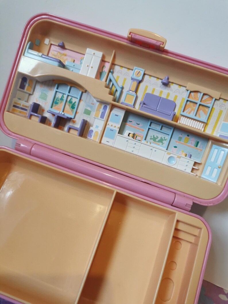 Puede incluir: Una casa de mu&ntilde;ecas de pl&aacute;stico rosa con una tapa extra&iacute;ble. La casa est&aacute; abierta y muestra el interior, que est&aacute; decorado con muebles y electrodom&eacute;sticos. La parte inferior de la casa tiene un compartimento de almacenamiento con dos secciones.