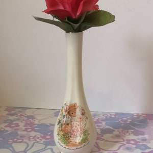 May include: A white ceramic vase with a floral design featuring a rabbit and the text "Friends who share are friends who care". A single red rose is in the vase.