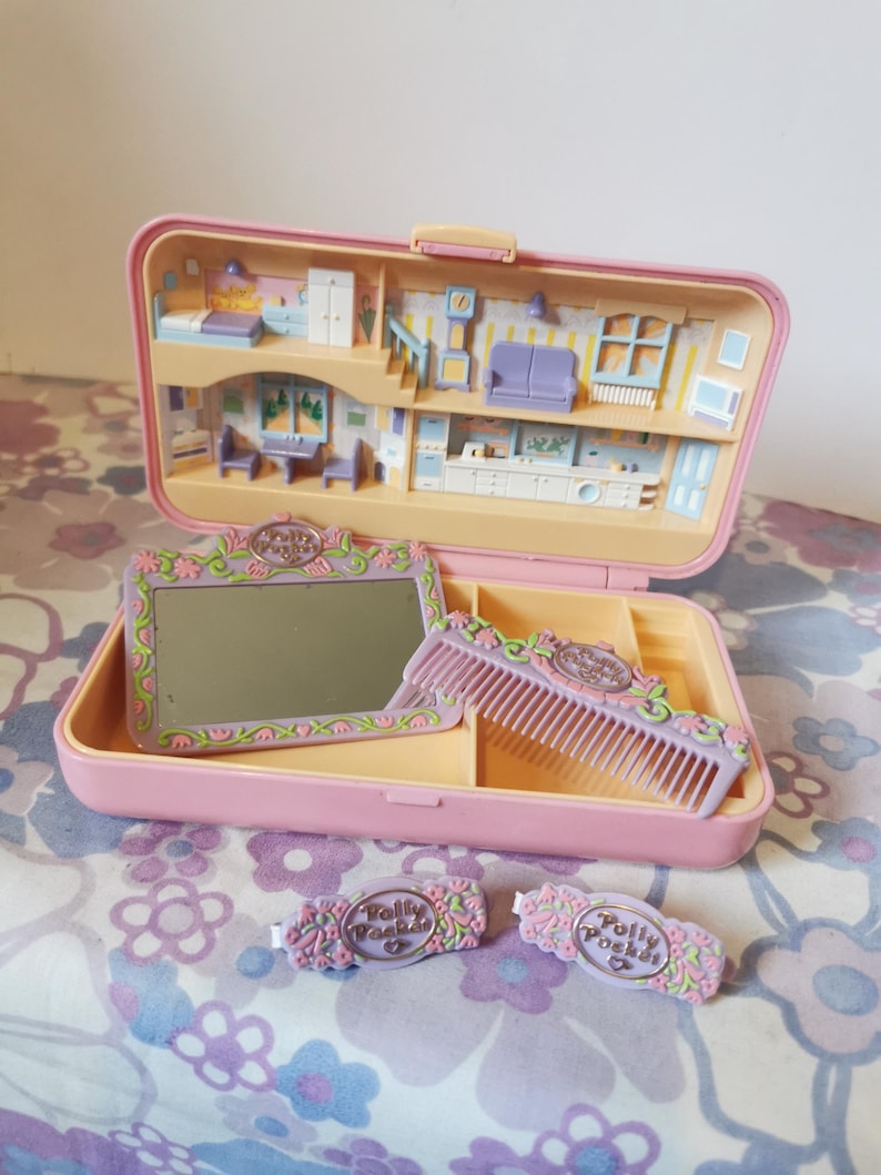 Puede incluir: Un estuche rosa Polly Pocket con un espejo, un peine y dos pinzas para el pelo. El estuche se abre para revelar una casa de mu&ntilde;ecas en miniatura con muebles y una cocina.