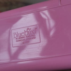 Puede incluir: Una caja de juguetes de pl&aacute;stico rosa con un logotipo de Bluebird Toys PLC y el s&iacute;mbolo de copyright 1990.