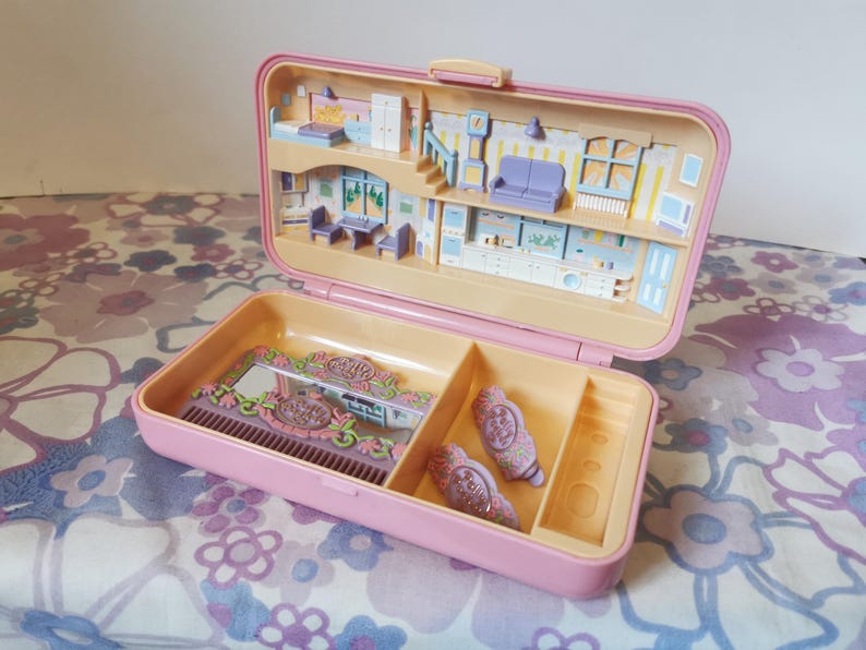 Puede incluir: Una casa de mu&ntilde;ecas de pl&aacute;stico rosa con un espejo, un peine y pinzas para el pelo. La casa tiene un dormitorio, una cocina y una sala de estar. La casa est&aacute; abierta y el interior es visible.