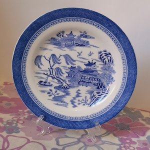 Könnte beinhalten: Ein blauer und weißer Keramikteller mit einem Weidenmuster. Der Teller hat einen blauen Rand mit einem sich wiederholenden Rautenmuster.