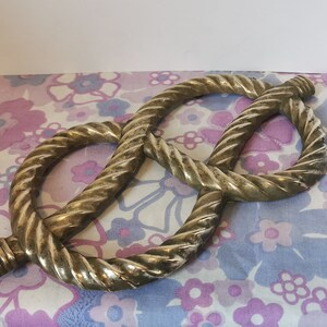 May include: A gold-coloured metal knot in the shape of a figure eight. The knot is on a floral patterned fabric.