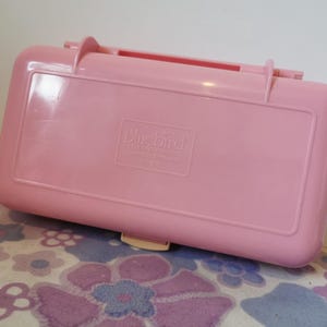 Puede incluir: Una caja de almacenamiento de pl&aacute;stico rosa con un cierre y un logotipo de Bluebird Toys. La caja est&aacute; vac&iacute;a.