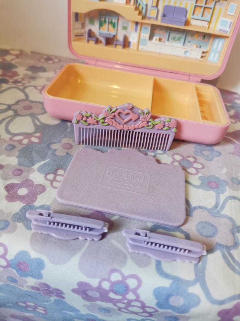 Puede incluir: Un peine de pl&aacute;stico morado con un dise&ntilde;o floral y un coraz&oacute;n en el centro. Hay dos pinzas para el pelo de pl&aacute;stico morado y una bandeja de pl&aacute;stico morado con las palabras "Bluebird Toys" impresas en ella.