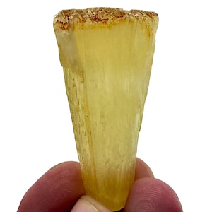 Puede incluir: Un mineral amarillo translúcido, similar a un cristal, con una punta puntiaguda y una superficie rugosa y texturizada.