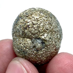 May include: A close-up of a pyrite specimen, also known as fool's gold, with a rounded shape. The surface is covered in small, reflective, cubic crystals, displaying a metallic gold color. The specimen has a slightly rough texture and a small indentation.
