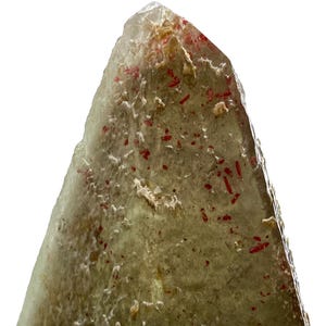 Puede incluir: Primer plano de un cristal transl&uacute;cido verde claro con inclusiones rojas. El cristal tiene una superficie rugosa y texturizada y una punta. Las inclusiones son peque&ntilde;as, dispersas y parecen ser de un tono rojo m&aacute;s oscuro.
