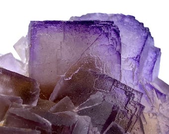 May include: A cluster of purple and brown fluorite crystals with a cubic structure. The crystals are translucent and have a glassy luster.