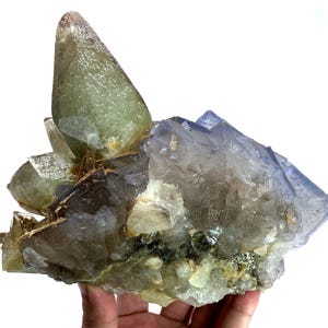 Puede incluir: Un grupo de cristales naturales en tonos verdes, azules y transparentes. Los cristales tienen una superficie rugosa y texturizada y est&aacute;n dispuestos en una formaci&oacute;n en capas. La apariencia general es la de una geoda o un esp&eacute;cimen mineral.