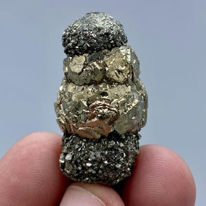 May include: A cluster of pyrite crystals, also known as fool's gold, in a stacked formation. The crystals are a metallic gold color with a rough, textured surface.