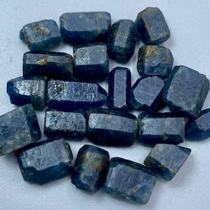 Könnte beinhalten: Eine Sammlung von rohen, dunkelblauen Saphirsteinen. Die Steine sind in verschiedenen Größen und Formen, einige haben einen leicht metallischen Glanz.