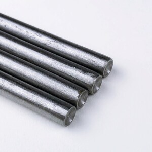 May include: Four silver metal rods stacked on top of each other on a white surface.