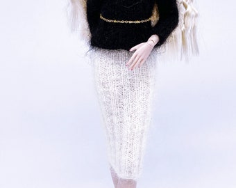 May include: A doll with long blonde curly hair wearing a black sweater with a gold chain belt and a white knitted skirt.