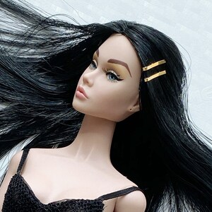 May include: A black mesh bodysuit with a sweetheart neckline. The doll has long black hair with gold barrettes.