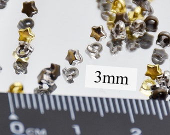 May include: A close-up of a pile of small, star-shaped metal studs in gold and silver tones. The studs are 3mm in size and are measured with a ruler.