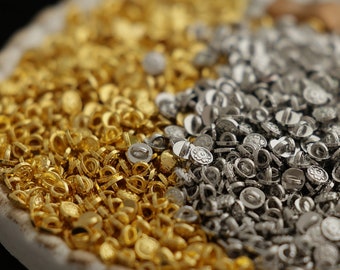 May include: A white ceramic dish with a brown ribbon and a pile of gold and silver metal eyelets.