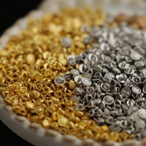 May include: A white ceramic dish with a brown ribbon and a pile of gold and silver metal eyelets.