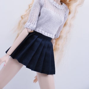 May include: A doll wearing a white knitted sweater and a black pleated skirt. The doll has long blonde hair and blue eyes.