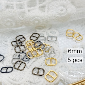 May include: A collection of small metal buckles in gold, silver, and black. The buckles are rectangular with a central bar. The image includes text that reads "6mm" and "5 pcs".
