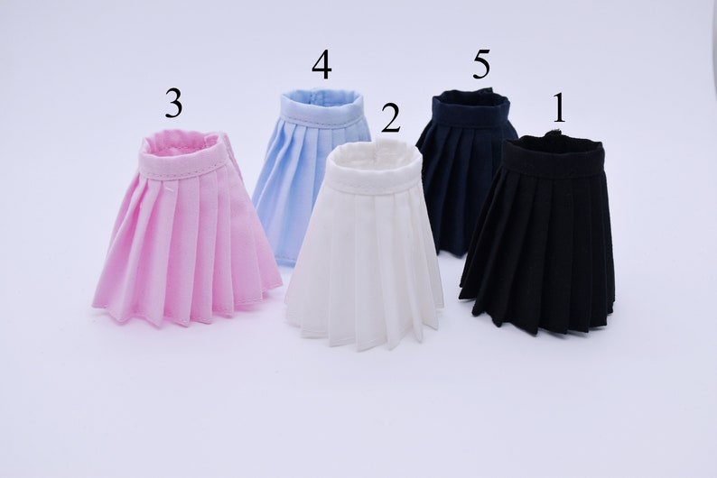 May include: Five pleated skirts in different colors: pink, light blue, white, navy blue, and black. The skirts are arranged in a row from left to right, with the pink skirt on the left and the black skirt on the right.