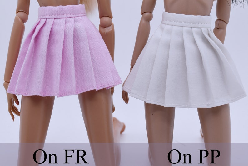 May include: Two pleated skirts, one pink and one white, are shown on doll-sized mannequins. The skirts are both short and have a simple design.