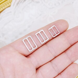 May include: Three silver metal slider buckles of different sizes. The buckles are rectangular with a small opening in the center.