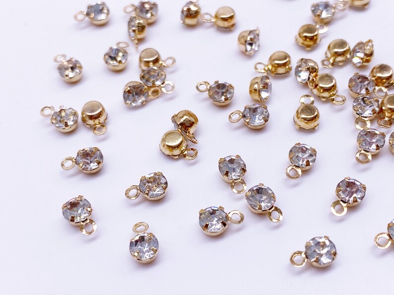 May include: A collection of gold-toned metal charms with clear crystal rhinestones. Each charm has a loop at the top and a small loop at the bottom.