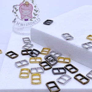 May include: Assortment of metal slider buckles in gold, silver, and bronze finishes. The buckles are small and have a rectangular shape with a center bar.