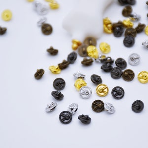 May include: Assortment of small, decorative metal buttons in gold, silver, and black. The buttons have a raised design and a circular shape.