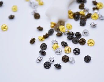 May include: Assortment of small, decorative metal buttons in gold, silver, and black. The buttons have a raised design and a circular shape.