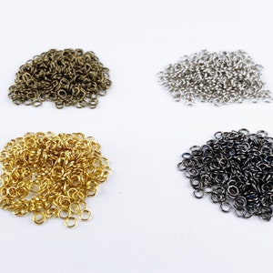 Può includere: Quattro pile di anelli di salto di diversi colori: oro, argento, bronzo e nero. Gli anelli di salto sono piccoli e rotondi, e sono tutti ammucchiati in un mucchio.