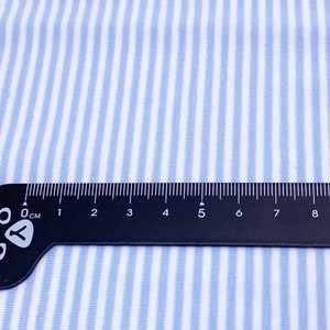 May include: A close-up of a blue and white striped fabric with a black ruler measuring 9 centimeters. The ruler has a cat paw design at the end.