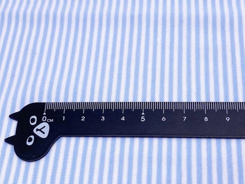 May include: A close-up of a blue and white striped fabric with a black ruler measuring 9 centimeters. The ruler has a cat paw design at the end.