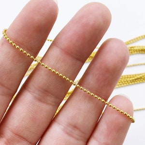 May include: A gold ball chain necklace with a delicate, fine chain. The chain is made of small, round beads that are evenly spaced.