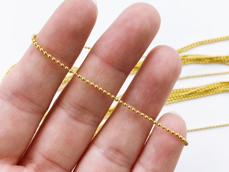 May include: A gold ball chain necklace with a delicate, fine chain. The chain is made of small, round beads that are evenly spaced.
