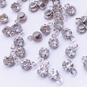 May include: A collection of silver-toned metal charms with clear crystal rhinestones. Each charm has a loop for attaching to jewelry or other crafts.