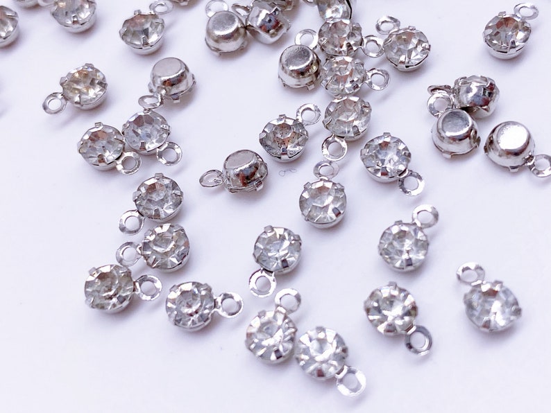 May include: A collection of silver-toned metal charms with clear crystal rhinestones. Each charm has a loop for attaching to jewelry or other crafts.