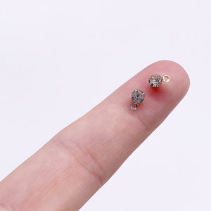 May include: Two small, clear rhinestone charms with gold-toned jump rings. The rhinestones are round and have a faceted finish.