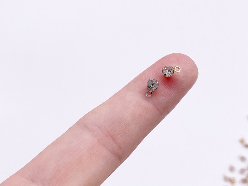 May include: Two small, clear rhinestone charms with gold-toned jump rings. The rhinestones are round and have a faceted finish.