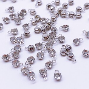 May include: A scattering of silver-toned metal charms with clear crystal rhinestones. Each charm has a loop for attaching to jewelry or other crafts.